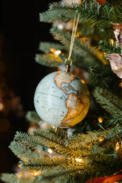 A toy globe on a Christmas tree on a festive yellow bokeh background. New Year\'s toys. Christmas mood.