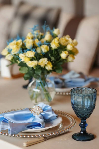 Birthday table decor. Blue glasses and napkins. Flowers on the table.