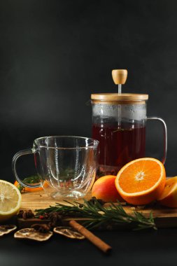 Fruit tea is poured into a transparent glass next to fruits on a black background.