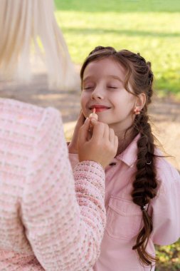 Bir anne parktaki çimlere kızının dudaklarını boyar. Mutlu bir çocuğun ilk makyajı..