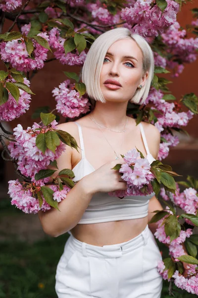 Bej arka planda kısa beyaz saçlı, seksi bir kadın ve çiçek açan bir sakura dalı..