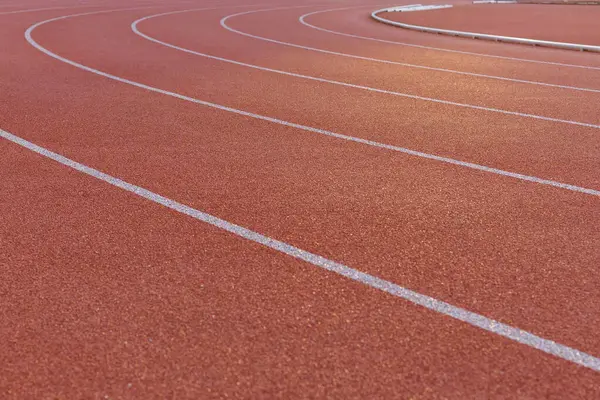 Close-up of the burgundy running track around the stadium illuminated by the morning light. Lines on a treadmill