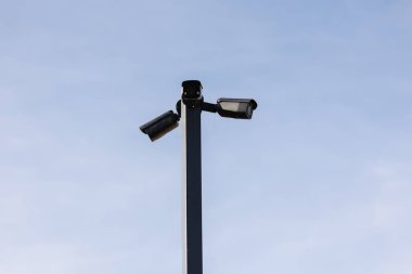 Dalgalı mavi gökyüzünün altında bir direğe monte edilmiş güvenlik kameraları var..