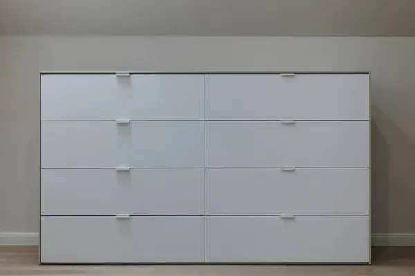 A detailed view of a sophisticated white dresser in a modern, all-white wardrobe space