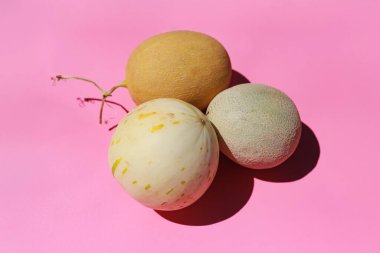 Pembe arka planda üç olgun kavun, canlı renklerini ve pürüzsüz dokusunu vurguluyor.