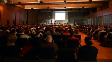 4K video of Science, Business and entrepreneurship symposium. Speaker giving a talk at scientific meeting. Audience in conference hall. Rear view of unrecognized participant in audience.