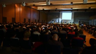 4K video of Science, Business and entrepreneurship symposium. Speaker giving a talk at scientific meeting. Audience in conference hall. Rear view of unrecognized participant in audience.
