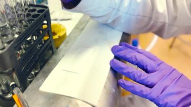 Bir kadın bilim adamı, reaksiyon sürecini izlemek için silis plaka üzerindeki ince katman kromatografisini kontrol ediyor. TLC plakasında 4K video pf örneği var.