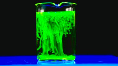 Koyu biyomedikal kimya laboratuarındaki cam konik şişede yeşil floresan solüsyonu deneyen bir kadın bilim adamı. 4K kopyalama uzayı.