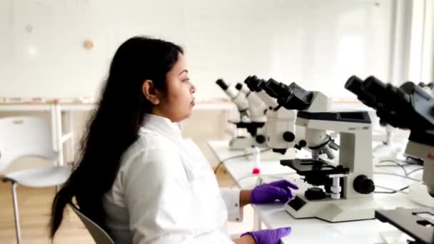 顕微鏡下のサンプルを調べる女性研究者 4Kマイクロバイオロジスト 技術機器を搭載した近代研究室で働く バイオケミストリー 医薬品 — ストック動画