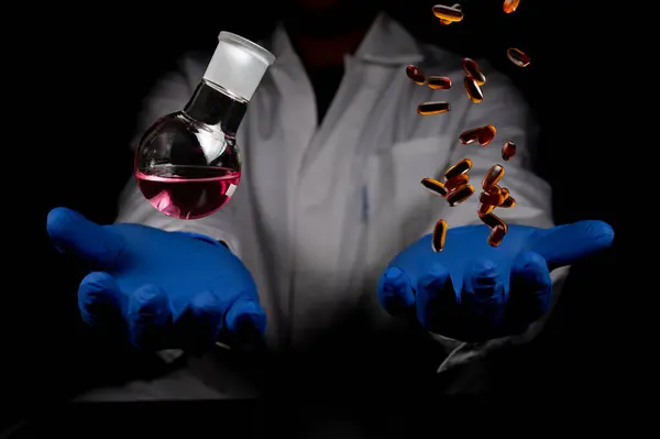 Chemistry round bottom flask and transparent pills dropping on a human scientist hand with black background copy space. Medicinal chemistry red chemical solution and chemical biology. chemisty laboratory and life.