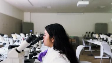 Kadın araştırmacı bilim adamı mikroskop altında örneklere bakıyor. Modern Laboratuvarda Teknolojik Ekipmanlarla çalışan 4K Mikrobiyolog. Biyokimya, ilaç..