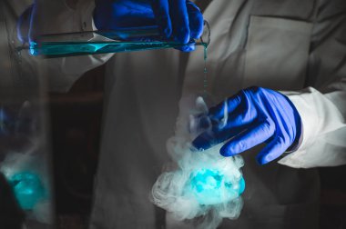 Mavi renk çözeltisiyle dumanlı deneyler. Kimyasal reaksiyon üzerinde çalışan bilim adamı cam şişeden yoğun duman çıkarıyor. Kopyalama alanı