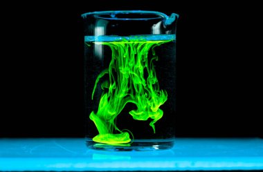 Dissolution and spread of a green substance in a flask with a clear liquid. Chemical reaction observed in the lab.. Copyspace. clipart