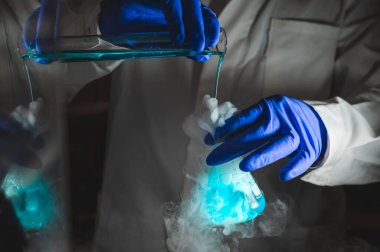 Mavi renk çözeltisiyle dumanlı deneyler. Kimyasal reaksiyon üzerinde çalışan bilim adamı cam şişeden yoğun duman çıkarıyor. Kopyalama alanı