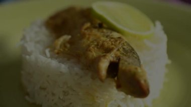 Tahta bir masada sarı bir tabakta servis edilen balık, pirinç ve limon dilimleri ile süslenmiş güzel bir yemek tabağı. Öğle ve akşam yemeği için Hint yemeği..