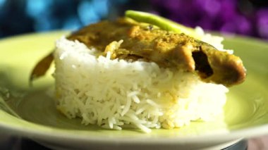 Tahta bir masada sarı bir tabakta servis edilen balık, pirinç ve limon dilimleri ile süslenmiş güzel bir yemek tabağı. Öğle ve akşam yemeği için Hint yemeği..