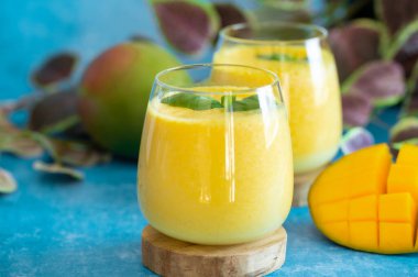 Mavi arka planda gözlüklü, fotokopi alanı olan taze mango Lassi. Hint sağIıklı zehirli ayurvedic soğuk içecek ve mango. Taze Lassi yoğurttan, sudan, baharatlardan, meyvelerden ve buzdan yapılır.