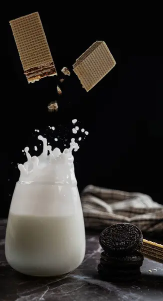 Milk Splash from biscuit fall in the glass on a black background. Dairy concept. No-dairy vegan plant milk splashes in glass. Copy space.