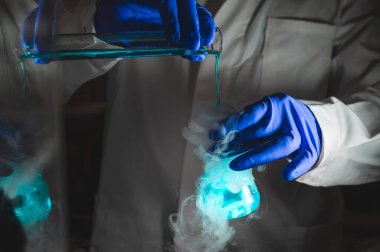 Mavi renk çözeltisiyle dumanlı deneyler. Kimyasal reaksiyon üzerinde çalışan bilim adamı cam şişeden yoğun duman çıkarıyor. Kopyalama alanı