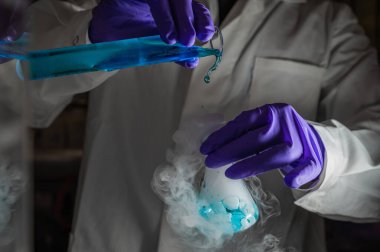 Mavi damlacıklarla yapılan dumanlı deneyler. Kimyasal reaksiyon üzerinde çalışan bilim adamı cam şişeden yoğun duman çıkarıyor. Kopyalama alanı