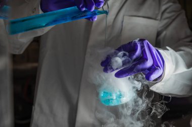 Mavi damlacıklarla yapılan dumanlı deneyler. Kimyasal reaksiyon üzerinde çalışan bilim adamı cam şişeden yoğun duman çıkarıyor. Kopyalama alanı