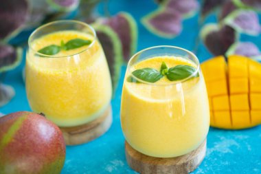 Fresh mango lassi in glasses on blue background with copy space. Indian healthy detoxic ayurvedic cold drink with mango. Freshness lassi made of yogurt, water, spices, fruits and ice clipart