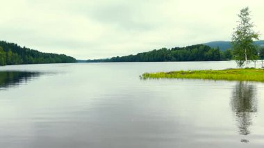 Yağmurlu ve bulutlu bir arazi manzarası. Çimenlerle dolu, kırmızı ahşap kulübeler ve yağmurlu bir günde gökkuşağı. Baharda bir açık hava ziyareti sırasında.