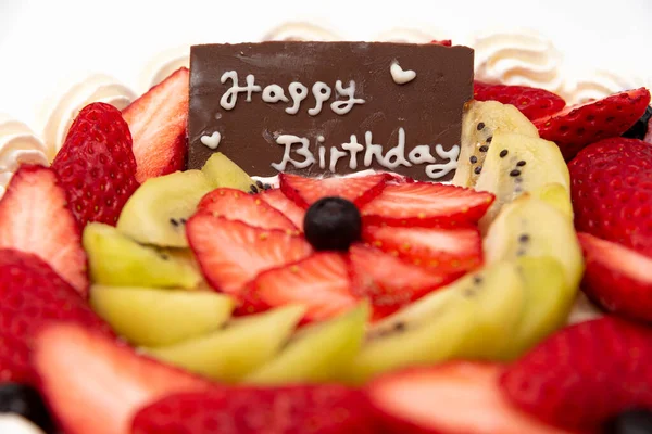 Homemade birthday cake decorated with strawberries, kiwi fruit and blueberries isolated on white background in side view and closeup.