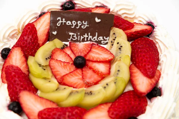 Homemade birthday cake decorated with strawberries, kiwi fruit and blueberries isolated on white background in side view and closeup.