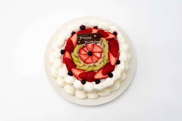 Homemade birthday cake decorated with strawberries, kiwi fruit and blueberries isolated on white background in top view.