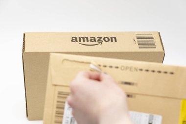 Fuji Şehri, Shizuoka-Ken, Japonya - 26 Mart 2023: Arka planda karton kutunun üzerindeki Amazon logosu üzerine seçici odaklı elden teslim zarfı. Kopya alanı ile beyaz arkaplanda izole.