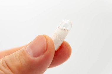 Beyaz arka planda izole edilmiş kapsülde bir kapsül tutan el..