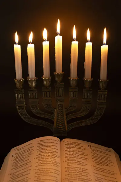 Holy Bible open to the Book of Isaiah in Chapter 11 and Menorah with 7 lit candles isolated on dark background.