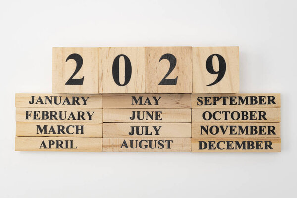 Year 2029 written on wooden cubes on top of the months of the year written on twelve rectangular pieces of wood. Isolated on white background.