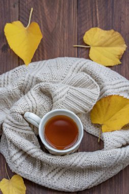 Yukarıdaki çay fincanından bej bir eşarp ve ahşap masa üzerinde sonbahar renkli yapraklar.