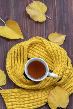 Yukarıdaki çay fincanından, ahşap masa üzerinde sonbahar renkli yaprakları olan sarı bir eşarpla çevrili.