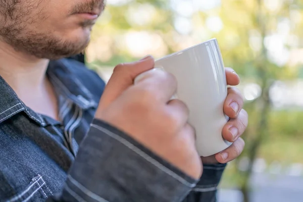 stock image man's hand holding a cup of coffee next to a window with autumn background outside