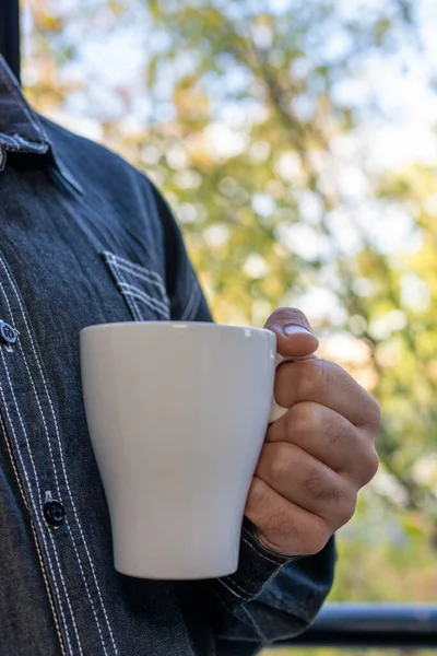男人的手捧着一杯咖啡 放在窗外 窗外是秋天的背景 — 图库照片