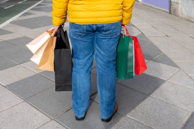 İki elinde de alışveriş torbası olan bir adam şehrin sokaklarında açık havada yürüyor.. 