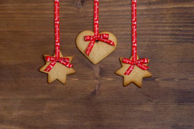 Kalp şeklinde zencefilli bisküviler ve yıldızlar, tipik Noel için, ahşap bir arka planda kırmızı bir kurdeleyle asılı, kopyalanmış spac