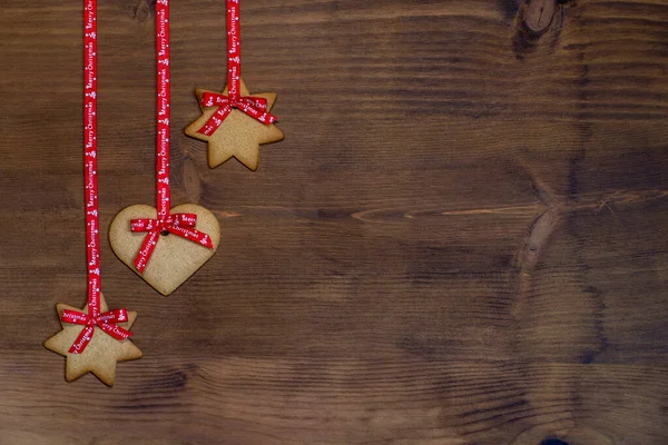 心と星の形でジンジャーブレッドビスケット クリスマスのために典型的な 木製の背景に赤いリボンで掛け スパックをコピーします — ストック写真