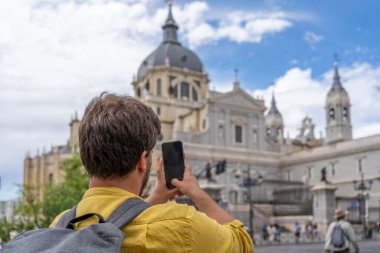 Sırt çantalı genç bir erkek öğrenci Madrid, İspanya 'daki Almudena Katedrali' nin kubbesinin telefonuyla fotoğraf çekerken eğleniyor.. 