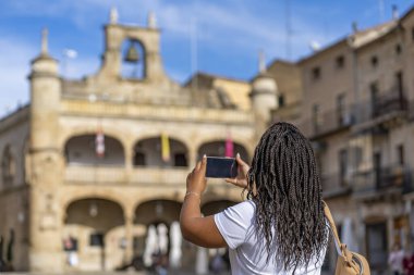 Büyük sırt çantalı kız fotoğrafçı kız Salamanca 'daki Ciudad Rodrigo' da 16. yüzyılın belediye binasının fotoğrafını çekiyor. Seyahat ve hobi kavramı