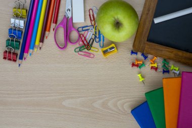 Not defterleri ve renkli resimlerle aydınlık ahşap masa manzarası diğer okul malzemelerini gösteriyor.