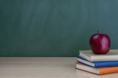 Masanın üzerinde kırmızı bir elma olan bir yığın kitap kara tahtanın yeşil arka planında yazıtlar için bir yer var..