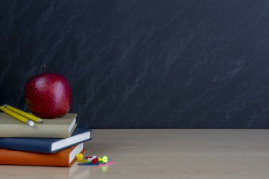 Bir yığın kitap, bir kırmızı elma ve renkli, okul malzemeleri, kara tahtanın siyah arka planında yazılar için bir yer var..