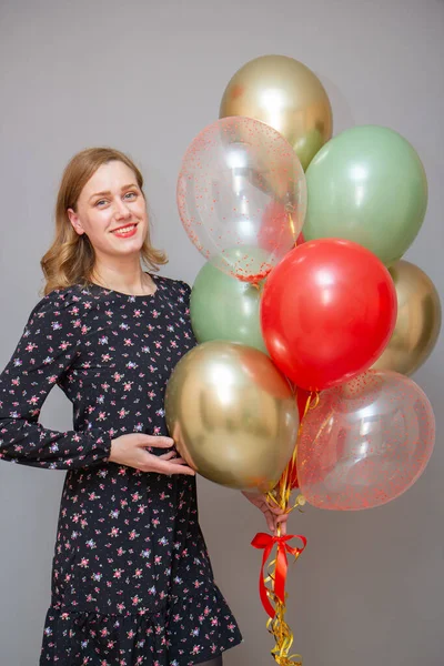 girl with red lipstick with a bunch of balloons against a gray wall