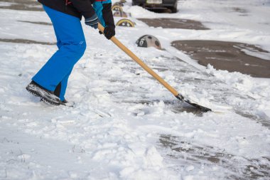child cleans snow with a shovel on a city street