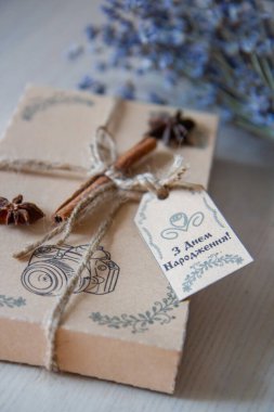 Kahverengi doğum günü hediyesi kutusunda tarçın çubuğu ve bir demet lavanta var.